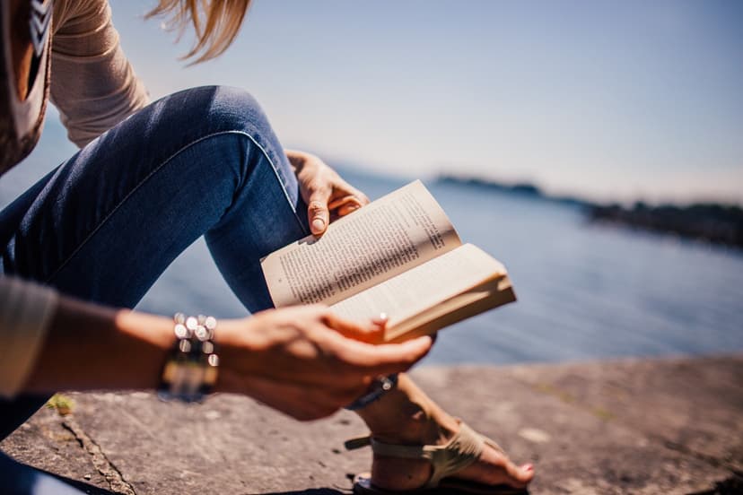 Kvinna på en sten vid vattnet och som läser i en bok